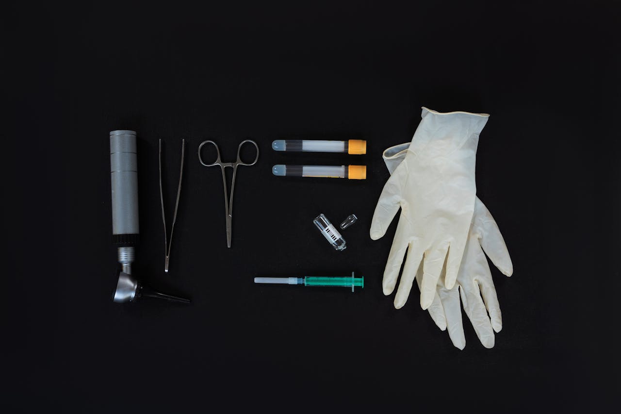 hero-img-01 Flat lay of essential medical tools on a black background, including gloves and syringe.