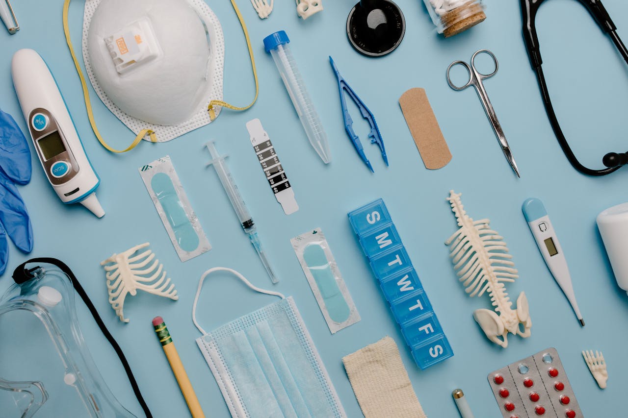 hero-img-02 A comprehensive flat lay of diverse medical supplies including PPE and diagnostic equipment on a blue surface.