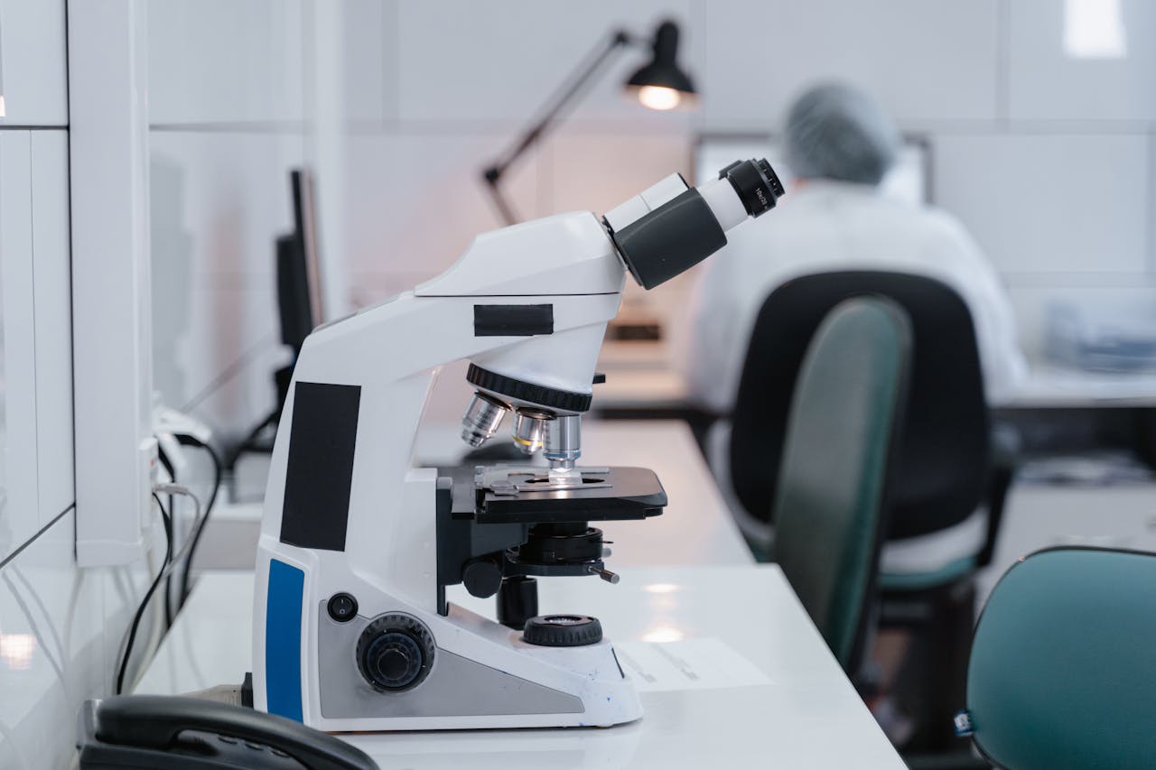 gallery-6 Close-up of microscope on desk in a modern laboratory with scientist working in the background.